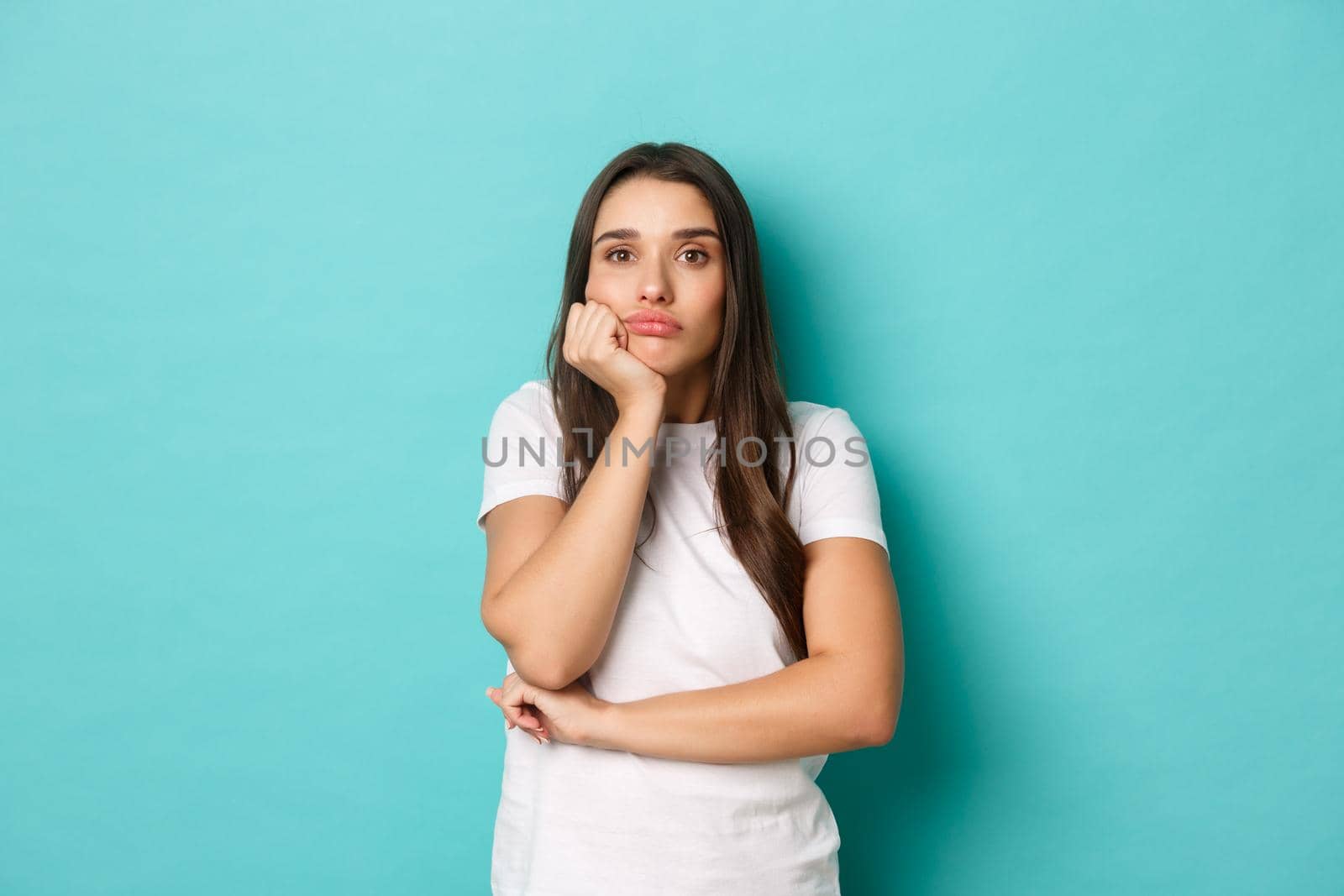 Sad and gloomy woman in white t-shirt, looking thoughtful into distance, standing over blue background by Benzoix