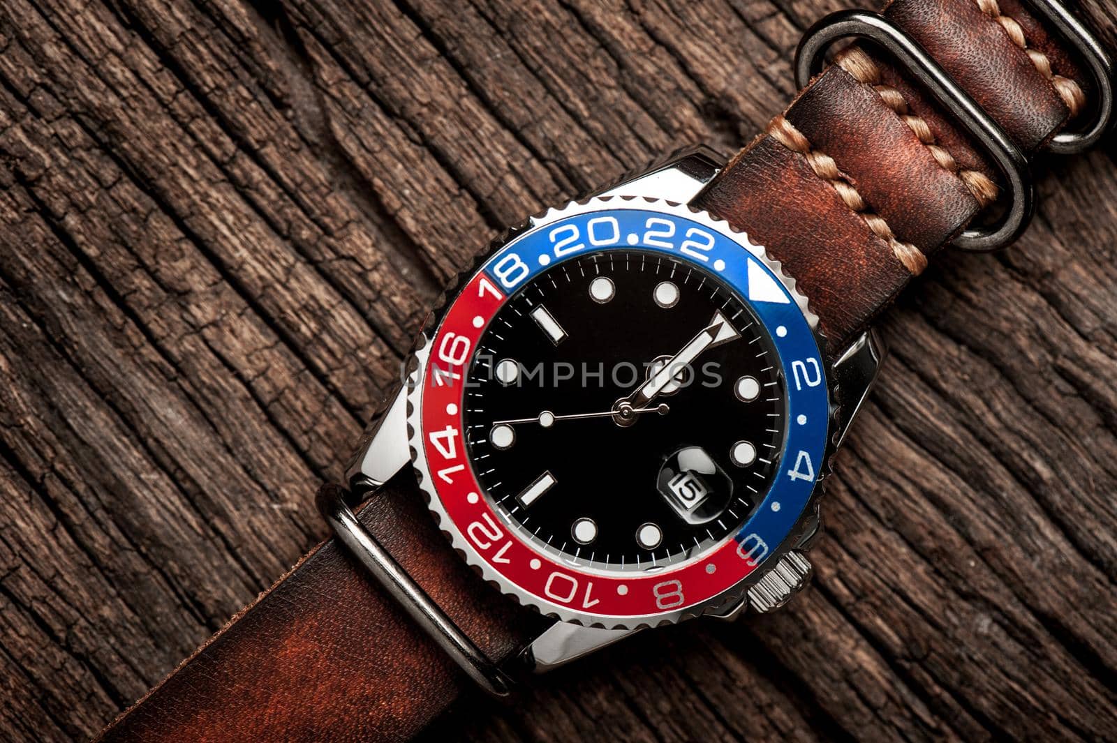 closeup luxury wristwatch for men with black dial blue-red bezel and leather strap.