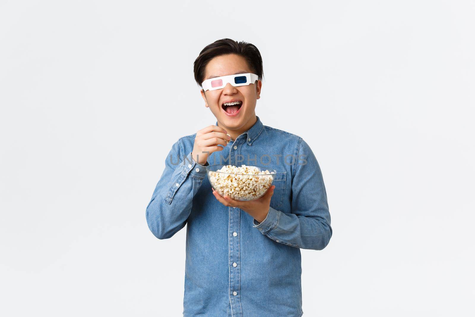 Leisure, lifestyle and people concept. Upbeat smiling asian guy in 3d glasses, eating popcorn and enjoying interesting movie, watching streaming service new tv series premier on awesome TV.