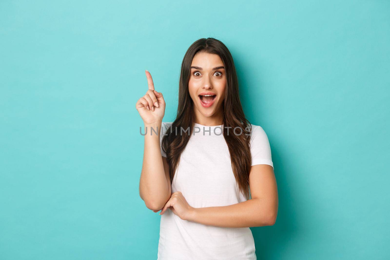 Image of pretty excited caucasian girl, having an idea, saying suggestion with finger raised up, standing in eureka pose over blue background.