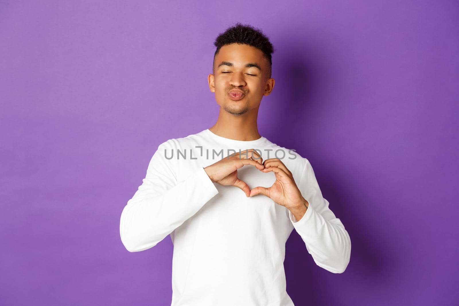 Image of lovely african-american boyfriend, waiting for kiss and showing heart sign, being in love, standing over purple background by Benzoix