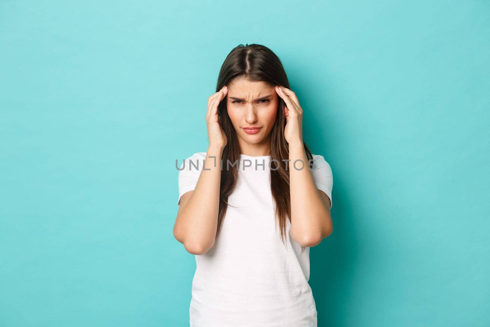Image of distressed young woman trying to focus, touching head and squinting, having headache, standing over blue background.
