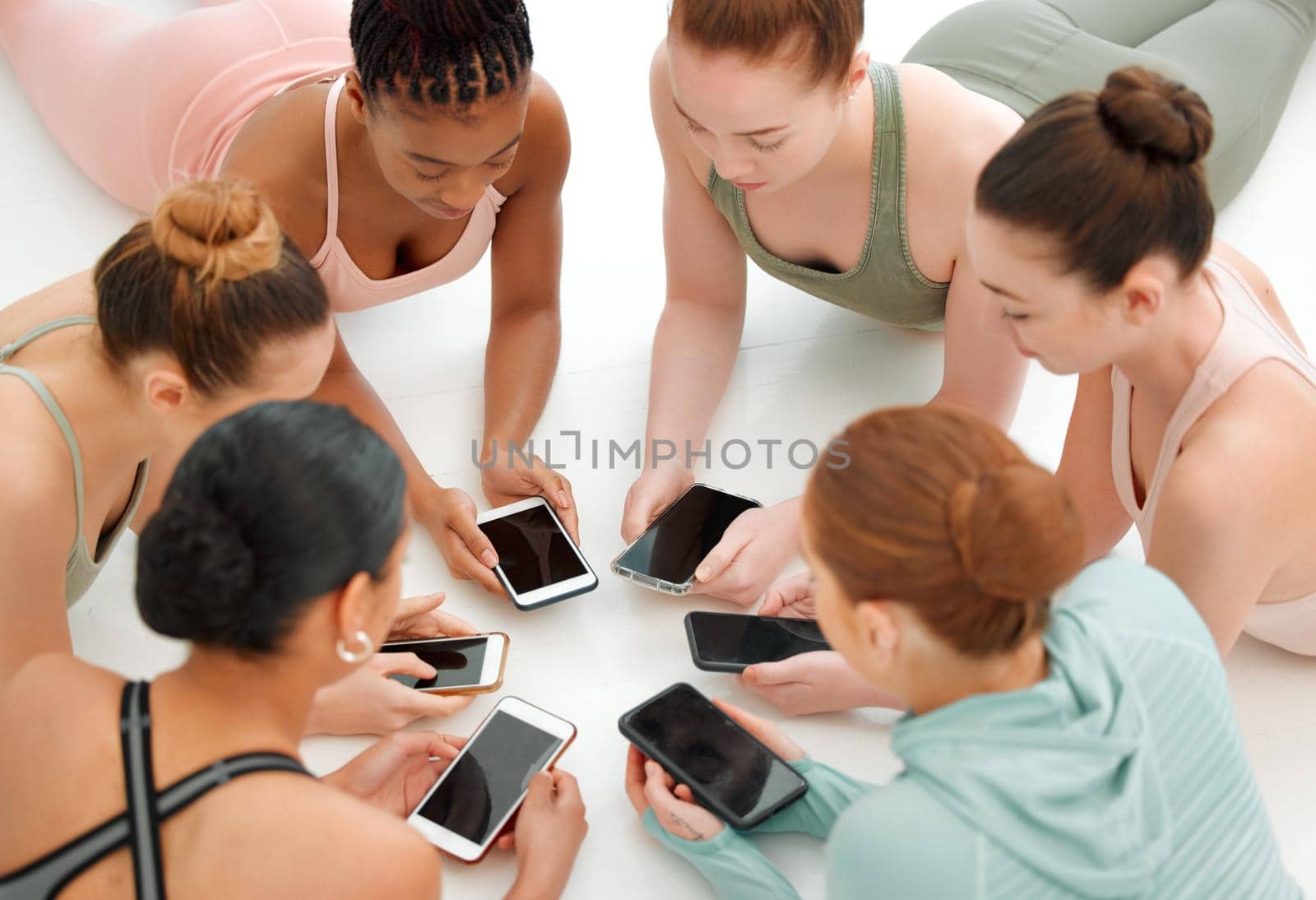 Fitness bloggers unite. a fitness group using their cellphones while in a circle. by YuriArcurs
