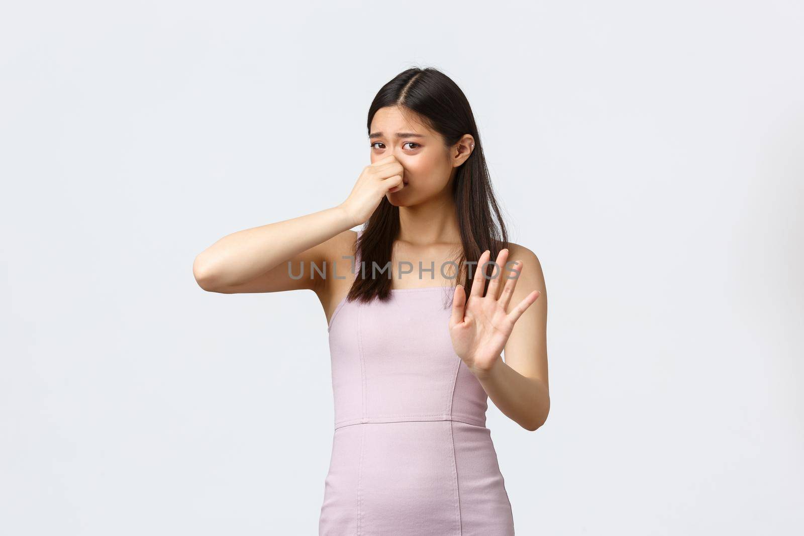 Luxury women, party and holidays concept. Disgusted young stylish asian woman in evening dress, shake hand in rejection or refusal or something stinky, shut nose from disgust, white background.