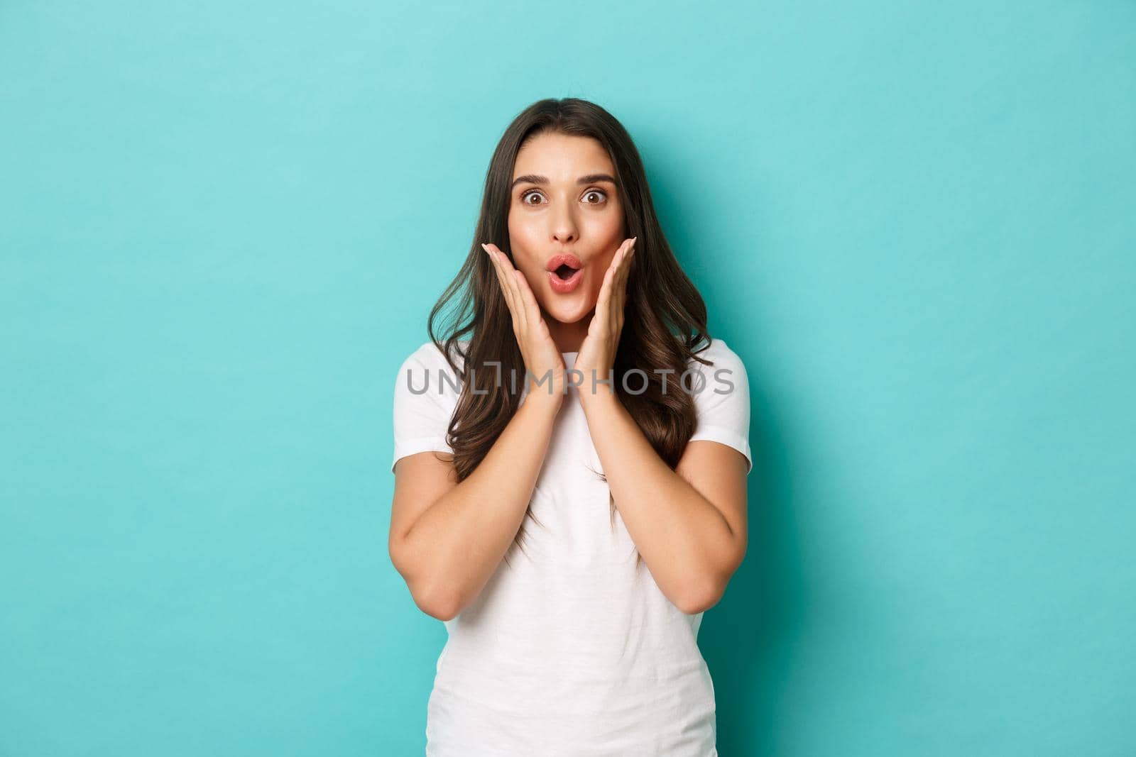 Image of surprised brunette girl reacting to announcement, gasping and looking at camera fascinated, gossiping over blue background by Benzoix
