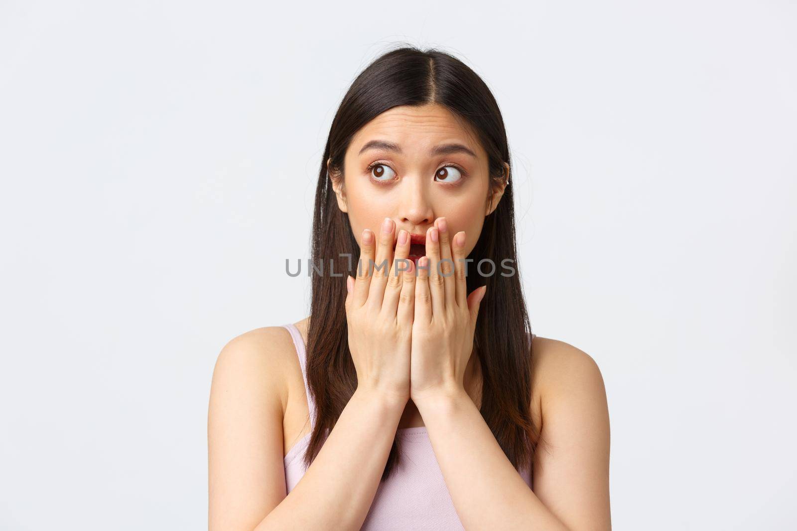 Beauty, fashion and people emotions concept. Shocked startled asian girl gasping, open mouth and cover it with palms, looking left astonished, standing concerned over white background by Benzoix