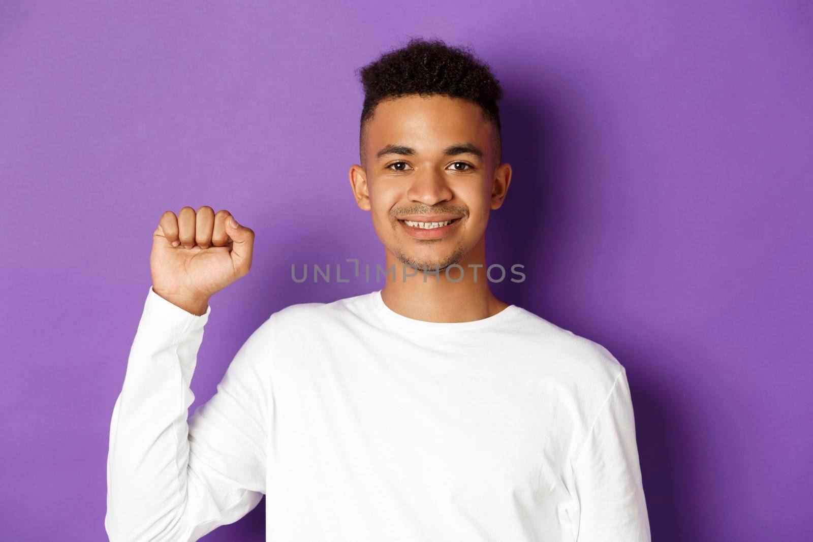 Close-up of handsome smiling african-american man, looking hopeful and raising fist, showing black lives matter sign, fighting for rights, standing over purple background by Benzoix