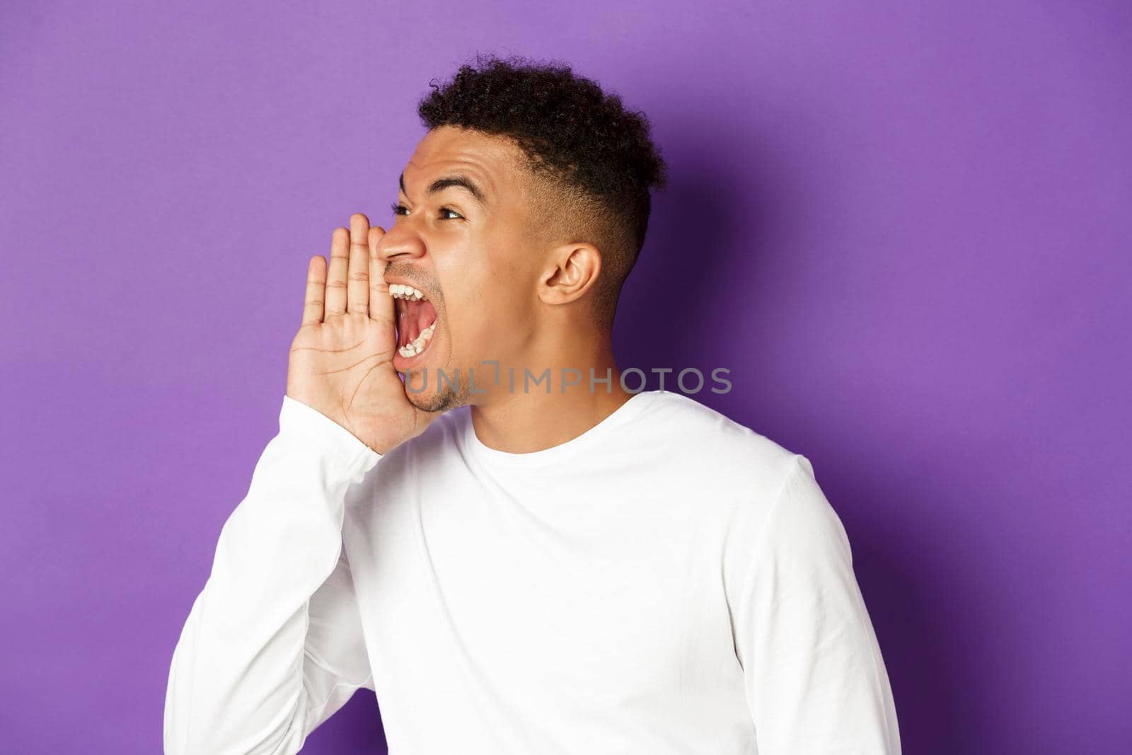 Image of african-american young man calling for someone, yelling and looking left, making loud announcement, standing over purple background.