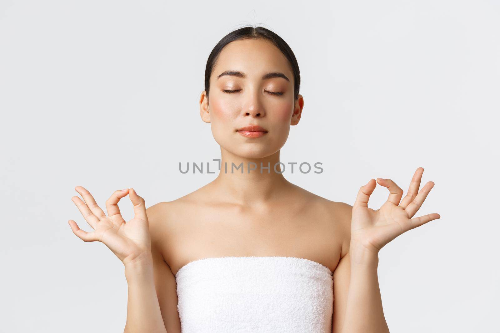 Beauty, cosmetology and spa salon concept. Close-up of meditating relaxed beautiful asian female in white towel make zen gesture with closed eyes, feeling pleased after massage therapy.