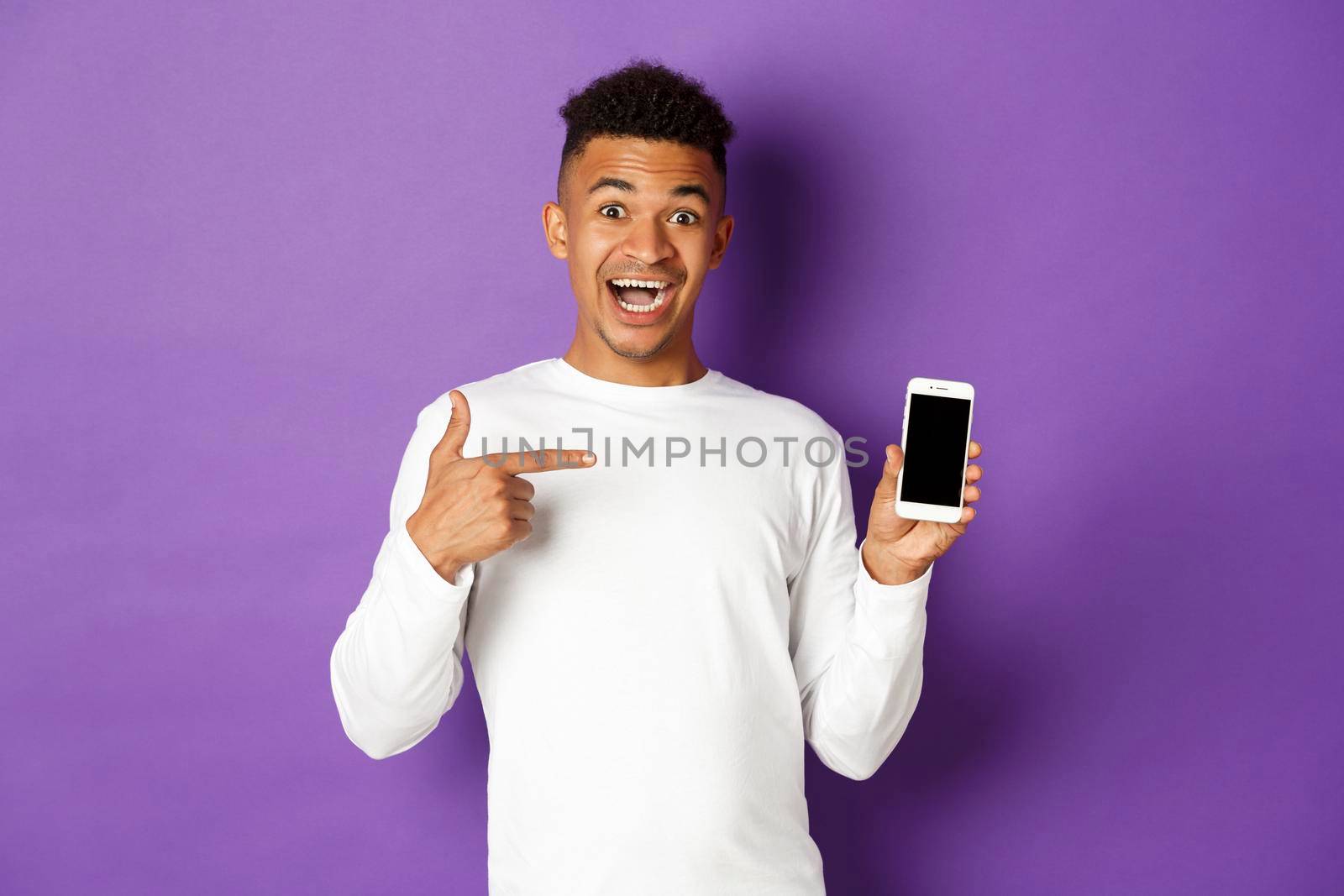 Handsome and excited african-american guy, pointing finger at smartphone screen, showing shopping site or app, standing over purple background by Benzoix