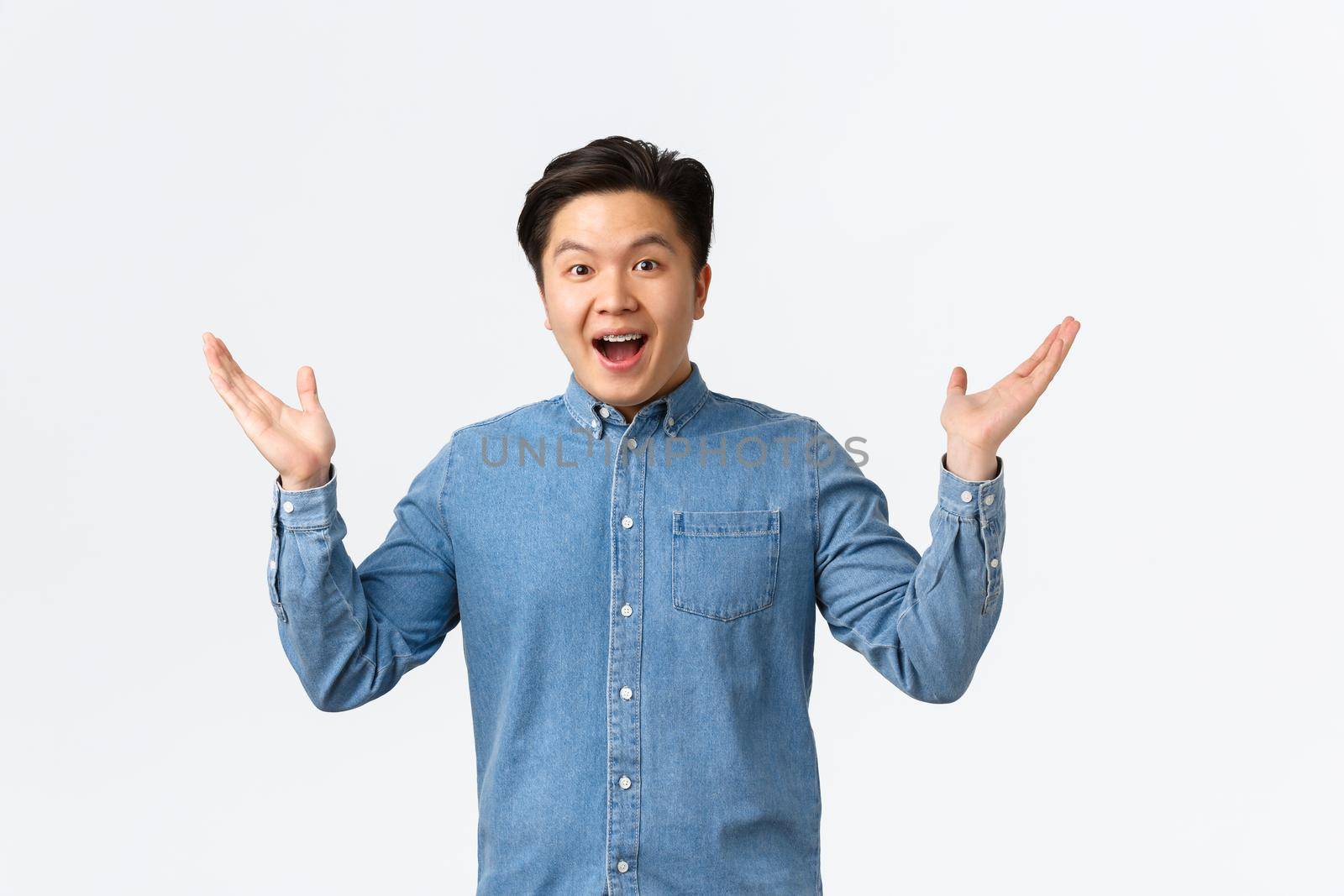 Happy and excited asian surprised guy receive awesome news, raising hands sideways and smiling amazed, praising great job, saying congrats, rejoicing over white background by Benzoix