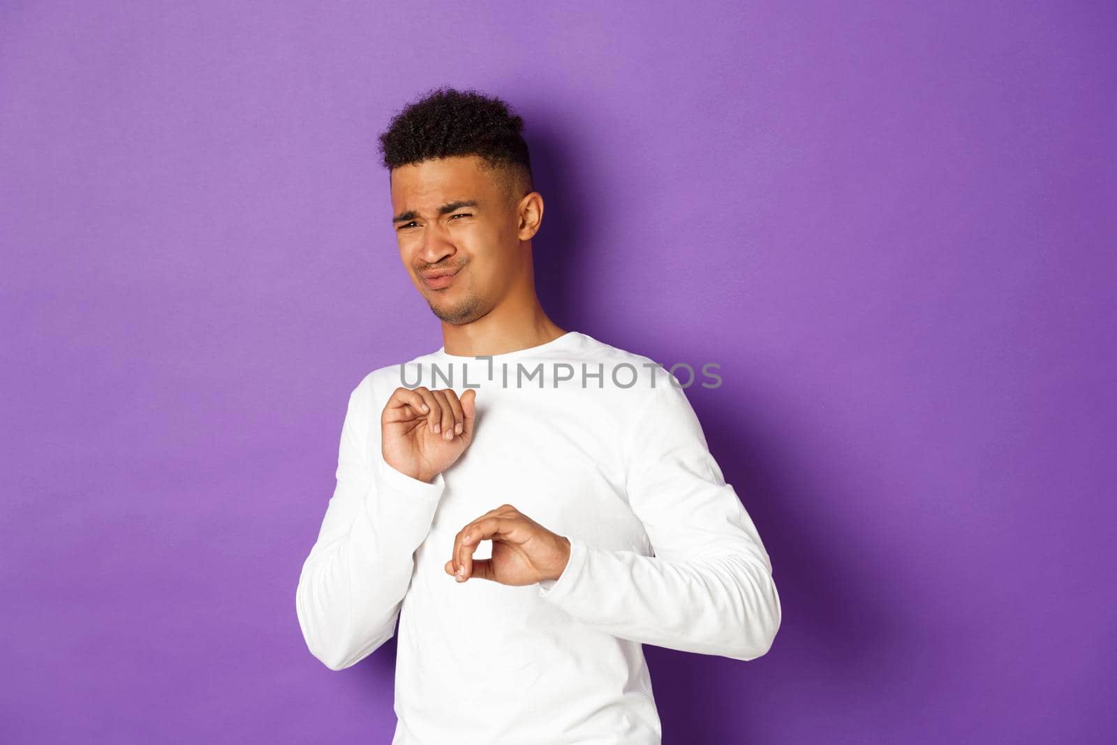 Image of young african-american guy cringe and looking at something disgusting, grimacing and standing over purple background by Benzoix