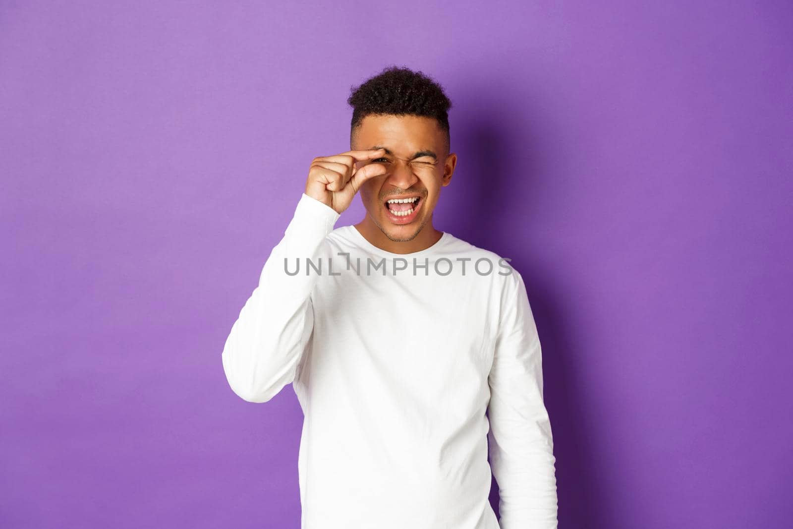 Happy african-american man showing something small, promote tiny thing, standing over purple background in white sweatshirt by Benzoix