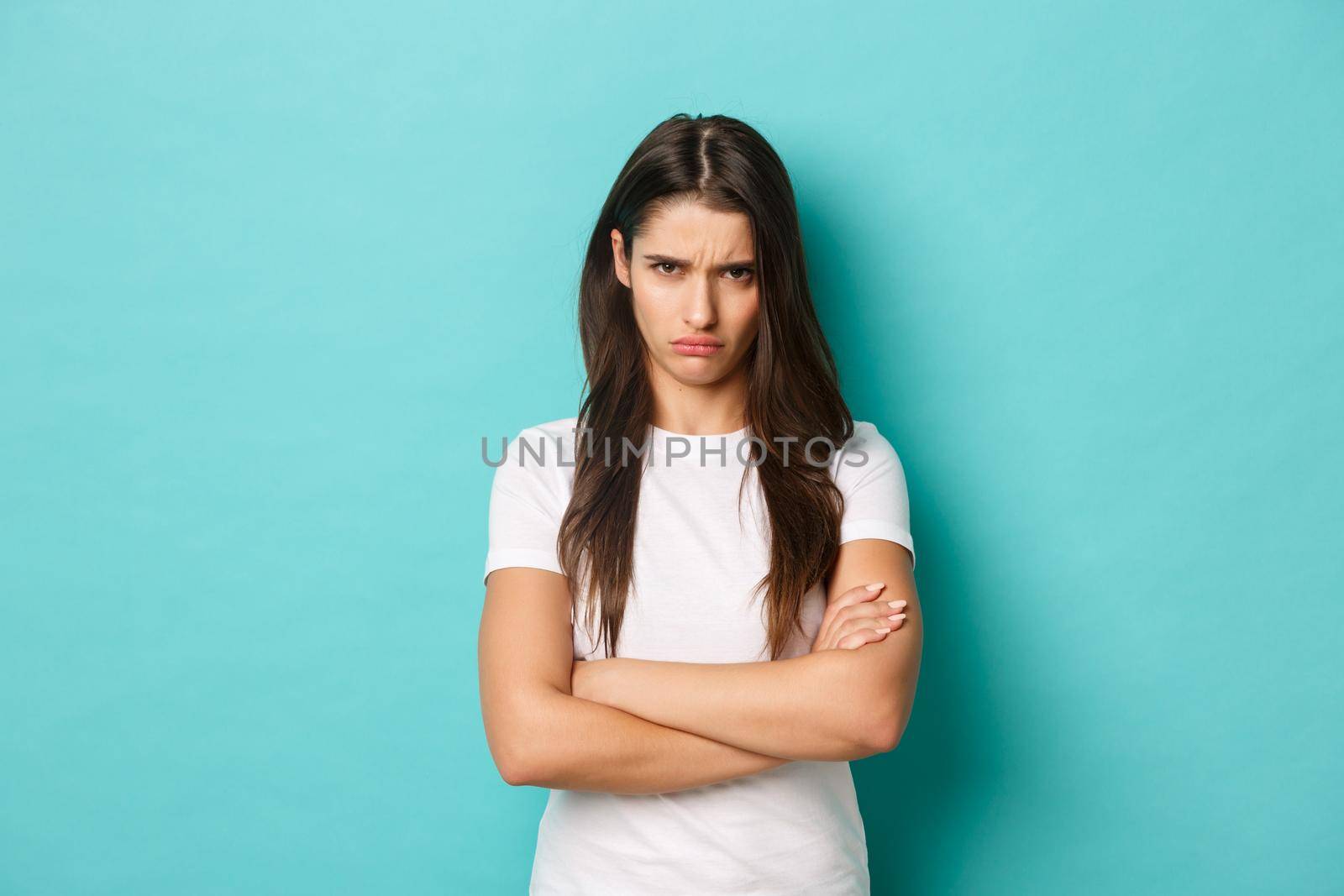 Image of upset sulking girl, feeling offended or jealous, cross arms chest and frowning angry, standing over blue background.