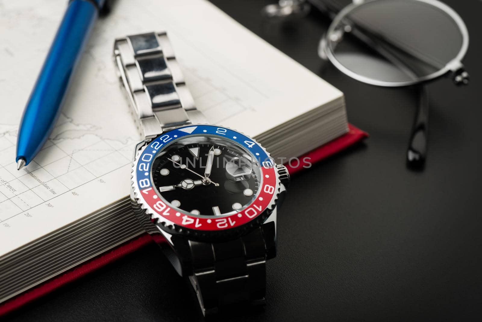 closeup luxury wristwatch for men with black dial blue-red bezel and stainless steel bracelet.