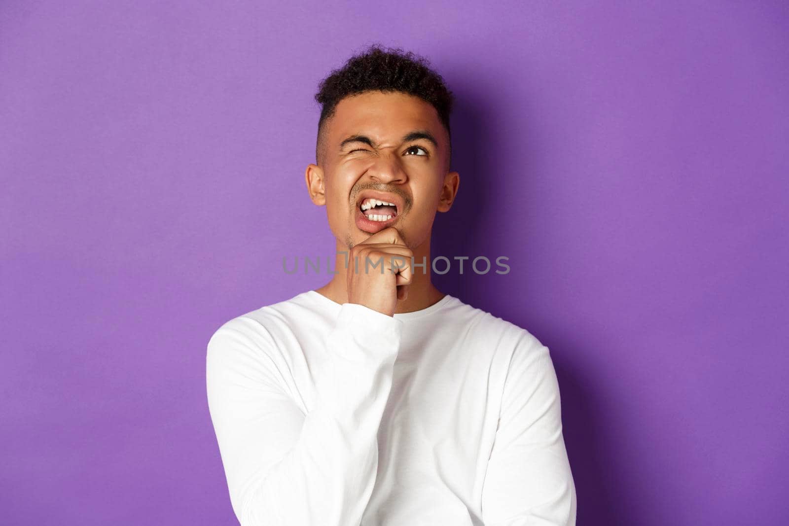 Close-up of thoughtful african-american man, making tough choice, looking up and thinking, standing over purple background by Benzoix