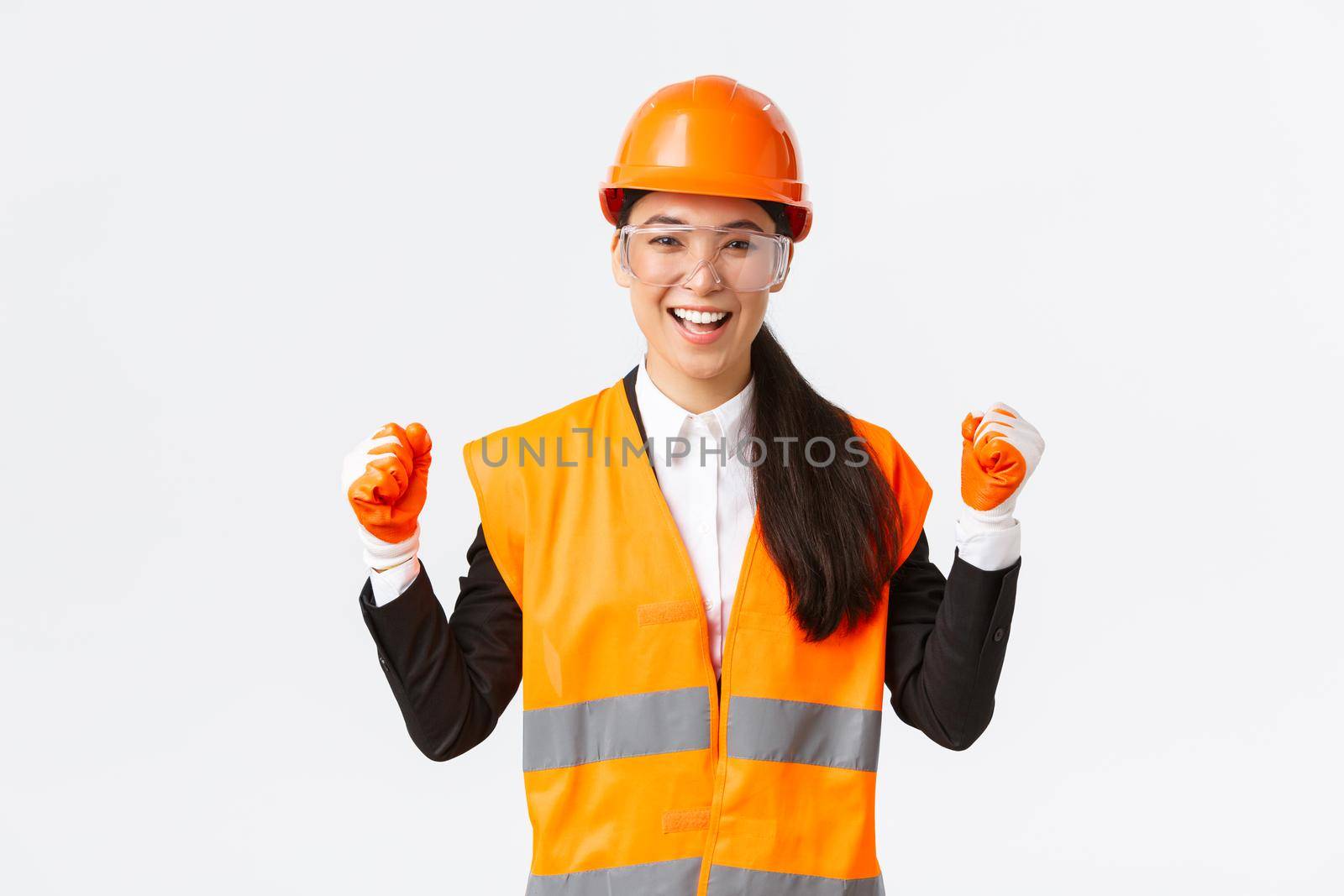 Successful winning female asian engineer, construction architect in protective glasses, gloves and helmet triumphing, fist pump rejoice and say yes, achieve goal, white background.