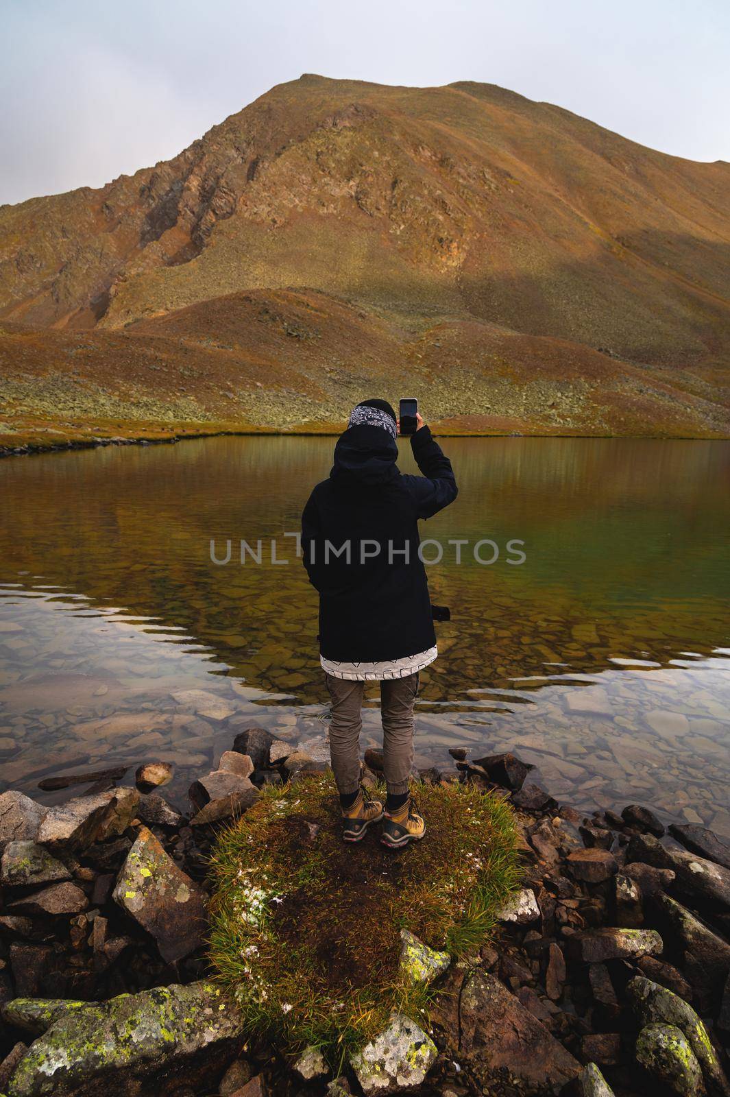 Travel photographer taking pictures of nature on a smartphone, mountain landscape by the lake. Tourist on adventure vacation by yanik88