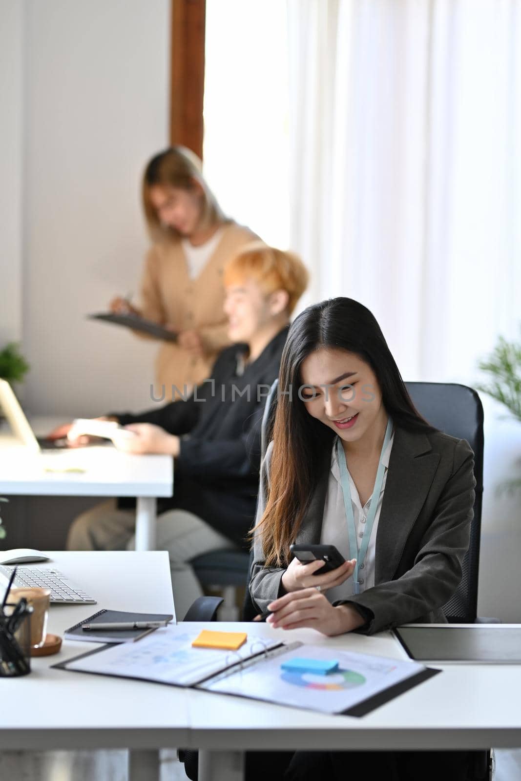 Portrait of charming businesswoman sitting in office and using smart phone.