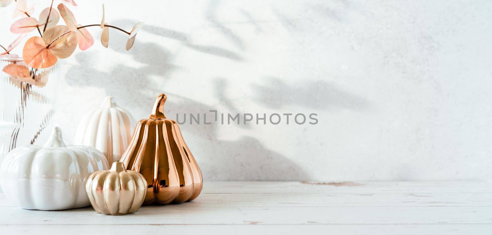 Details of Still life, cup of tea or coffee, pumpkins, candle, brunch with leaves on white table background, home decor in a cozy house. Autumn weekend concept. Fallen leaves and home decoration. by Ostanina