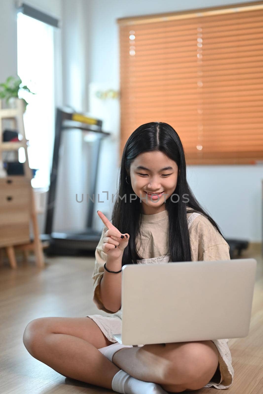 Smiling asian woman having video call with laptop computer while sitting on floor in living room.