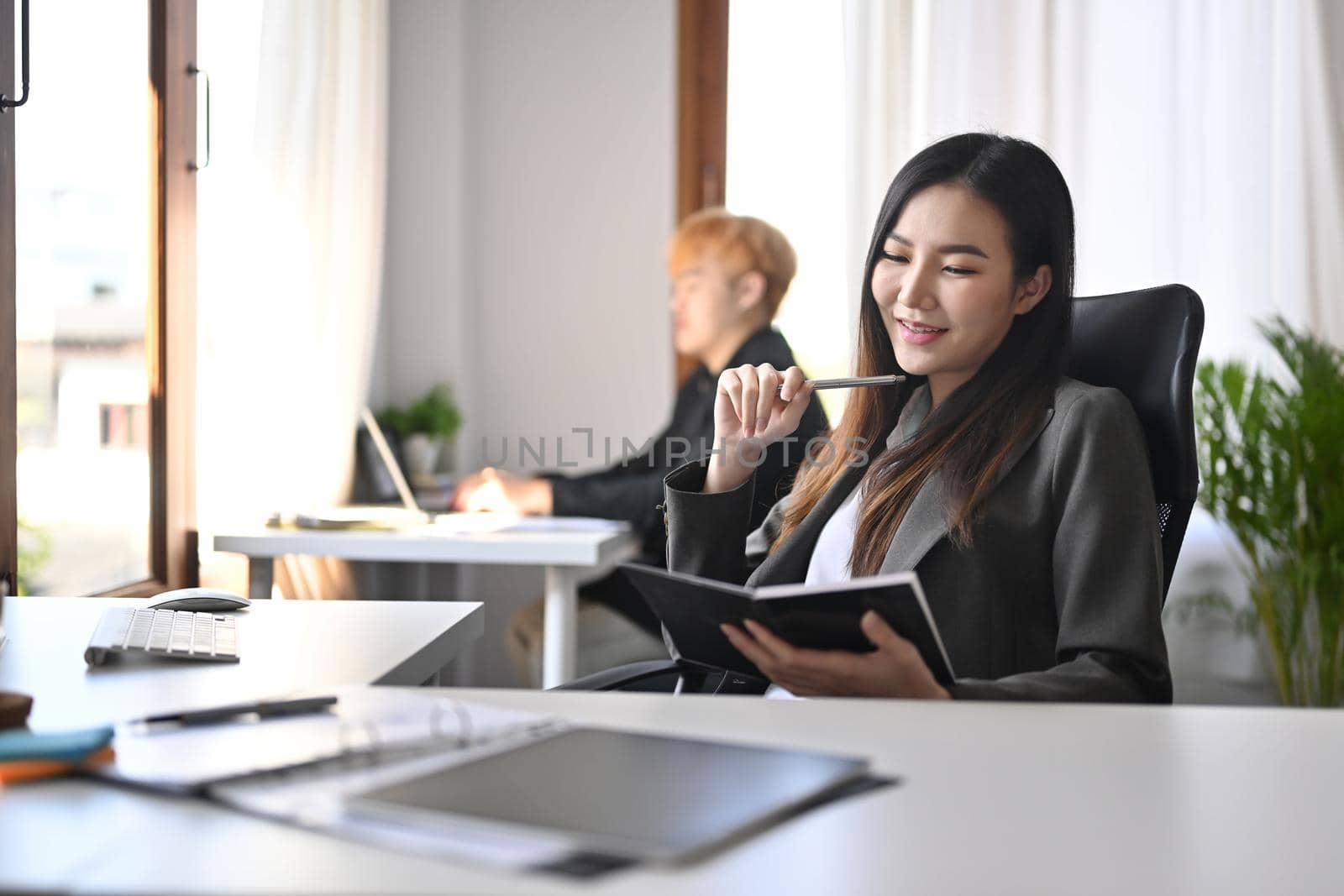 Beautiful businesswoman sitting on comfortable office chair and reading book. by prathanchorruangsak