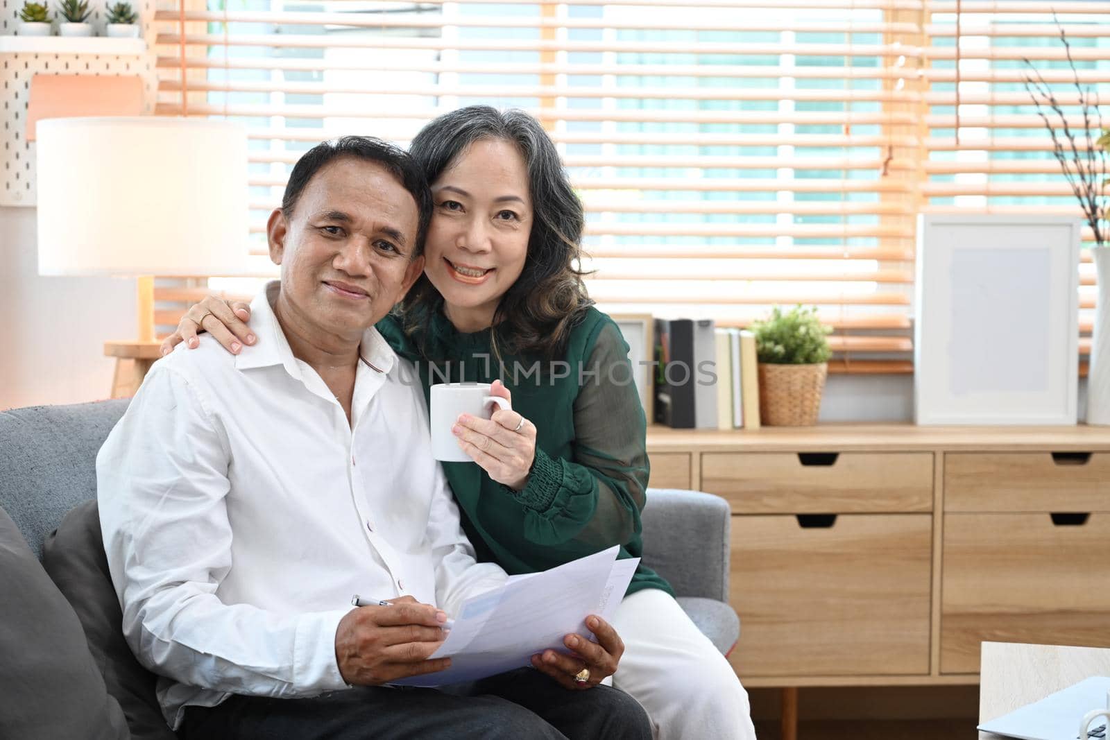 Happy senior couple relaxing together on comfortable sofa at home. Retirement lifestyle concept by prathanchorruangsak