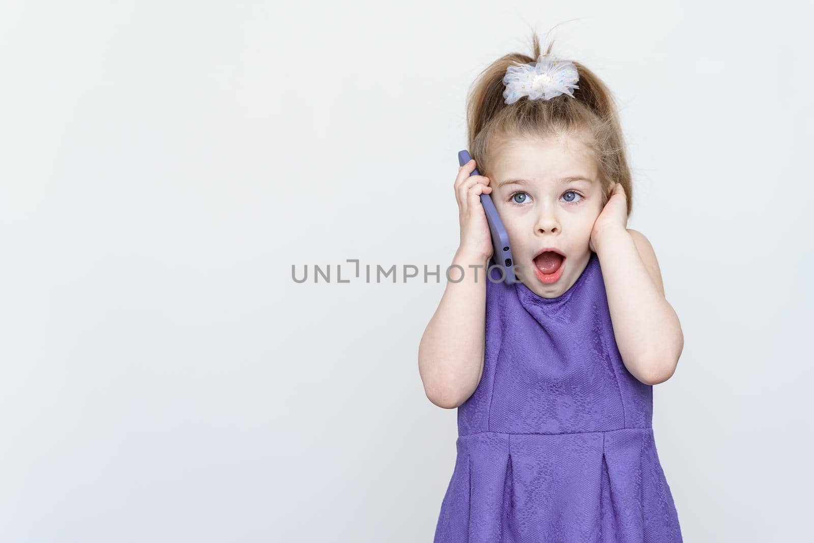 emotional 5-6 year old girl in a blue dress posing in the studio with a smartphone by Lena_Ogurtsova