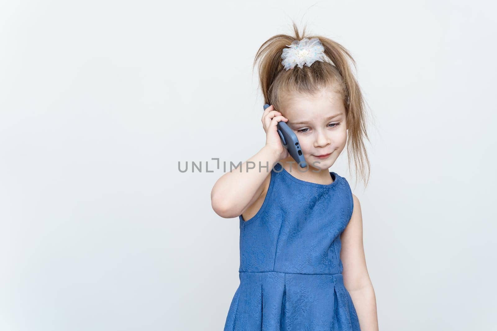 cute 5-6 year old girl in a blue dress posing in the studio with a smartphone