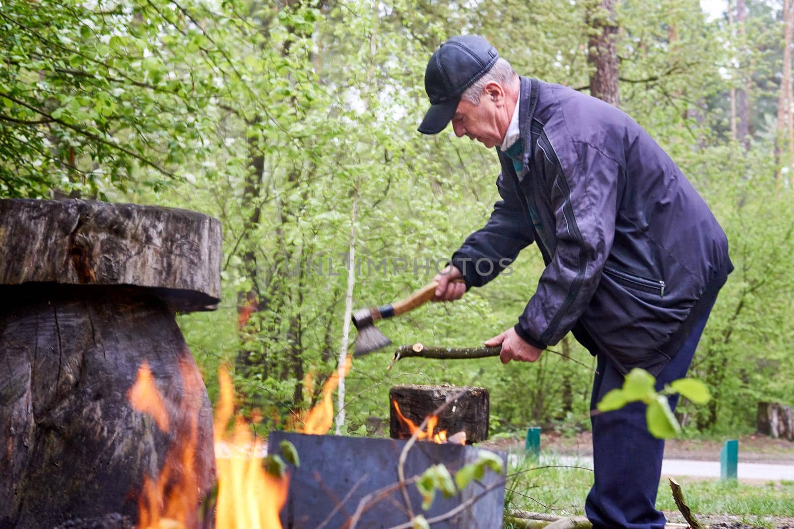 Elderly cheerful man pensioner chopping wood for a fire on vacation at a picnic by jovani68