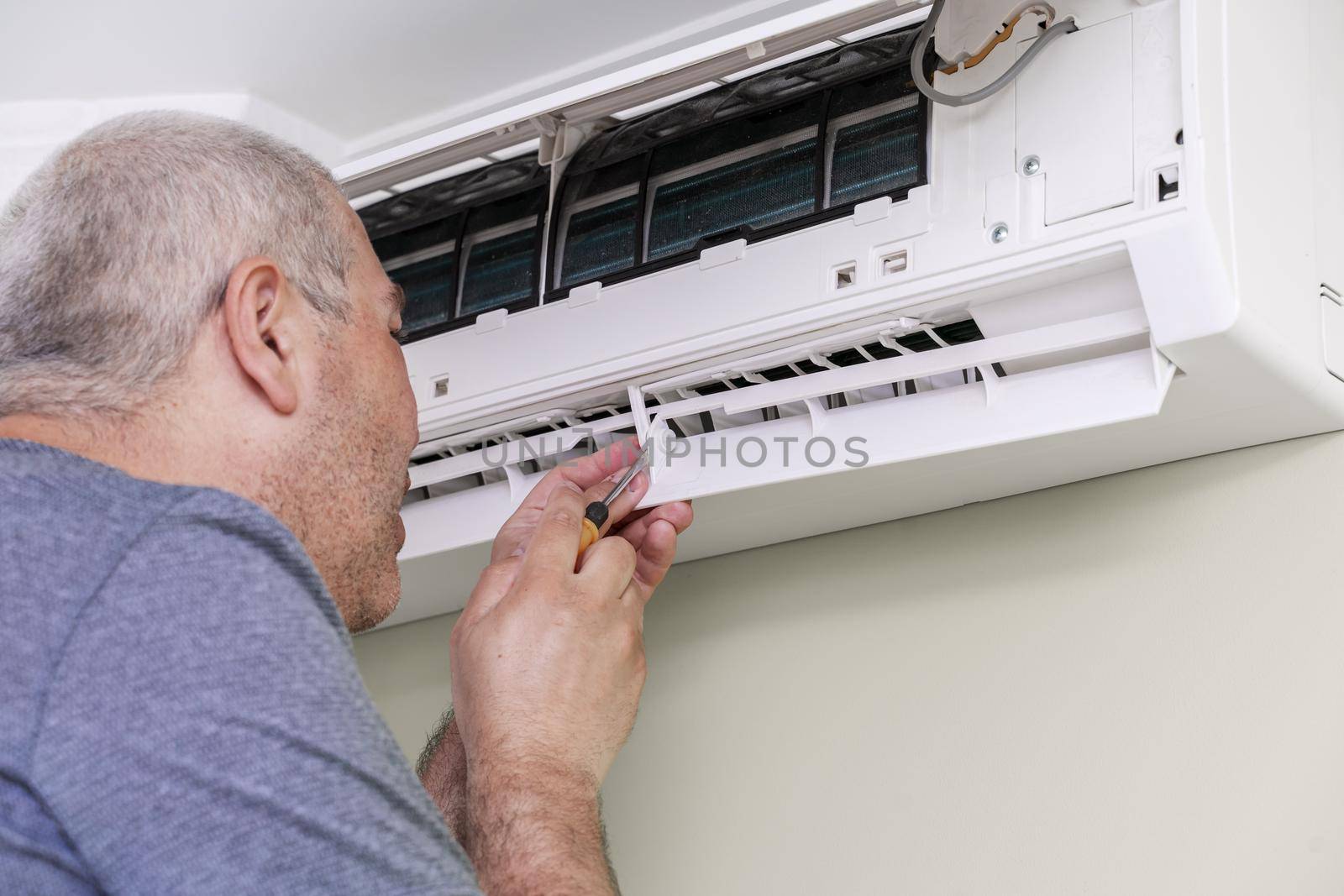man using screwdriver to repairing air conditioner indoors