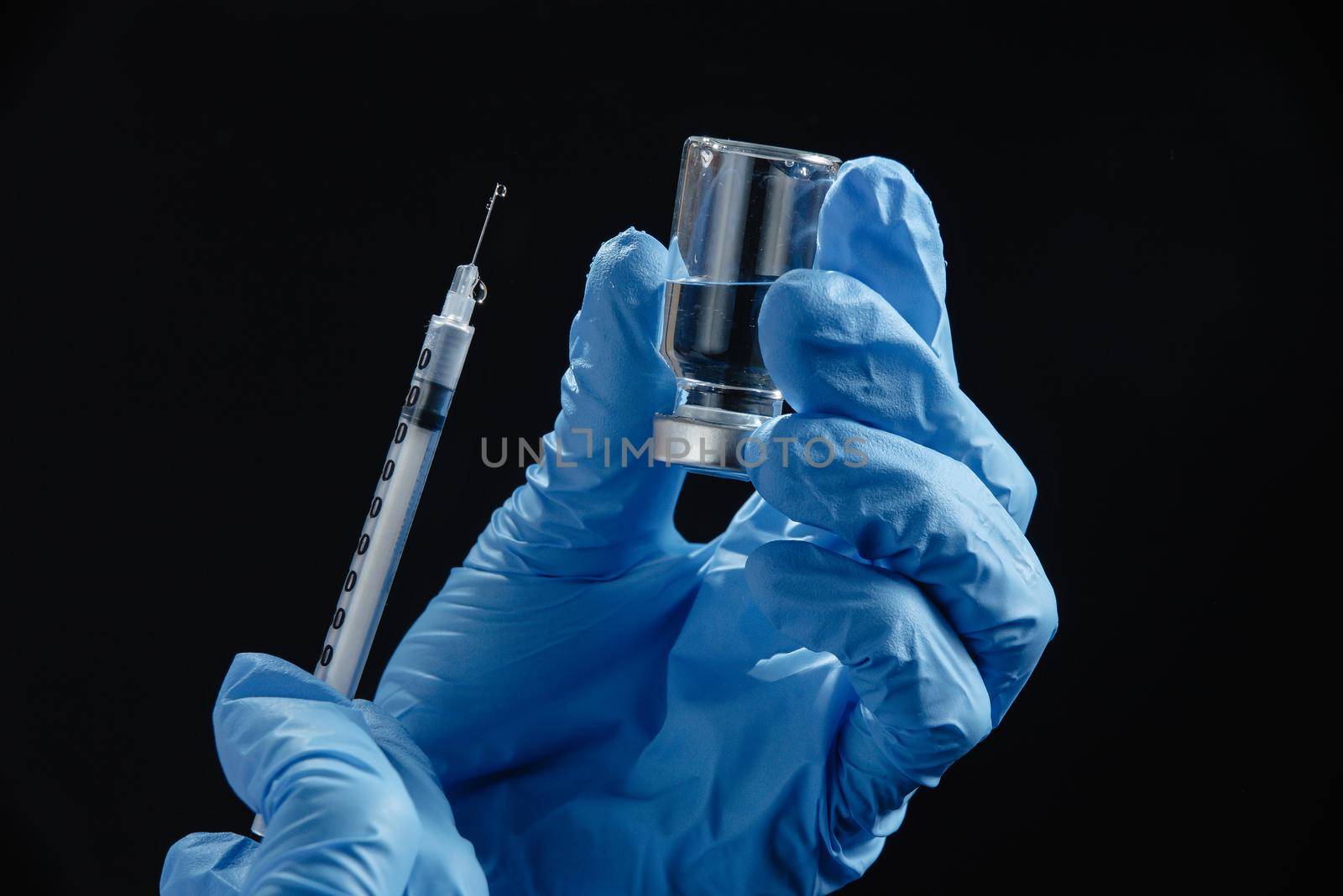 the doctor's hands hold a syringe of liquid vaccine against a black background. A doctor or scientist in the COVID-19 medical vaccine research and development laboratory holds a syringe with a liquid vaccine to study and analyze antibody samples for the patient