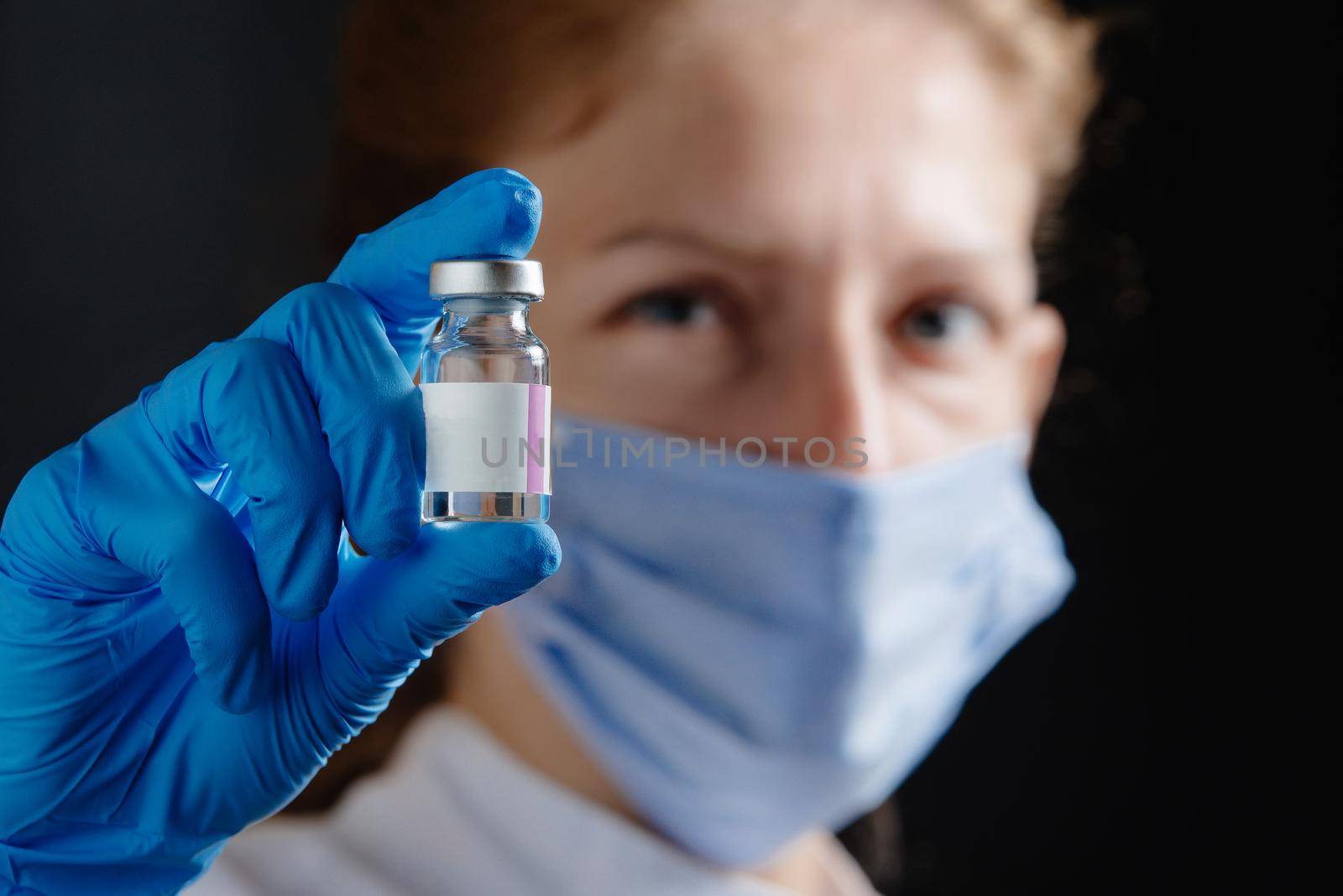 A female doctor or nurse is holding a test tube of medicine. Physician holding a test tube and blue protective medical gloves on a black background. Vaccine from Omicron. Medical doctor holds vaccine for a patient.