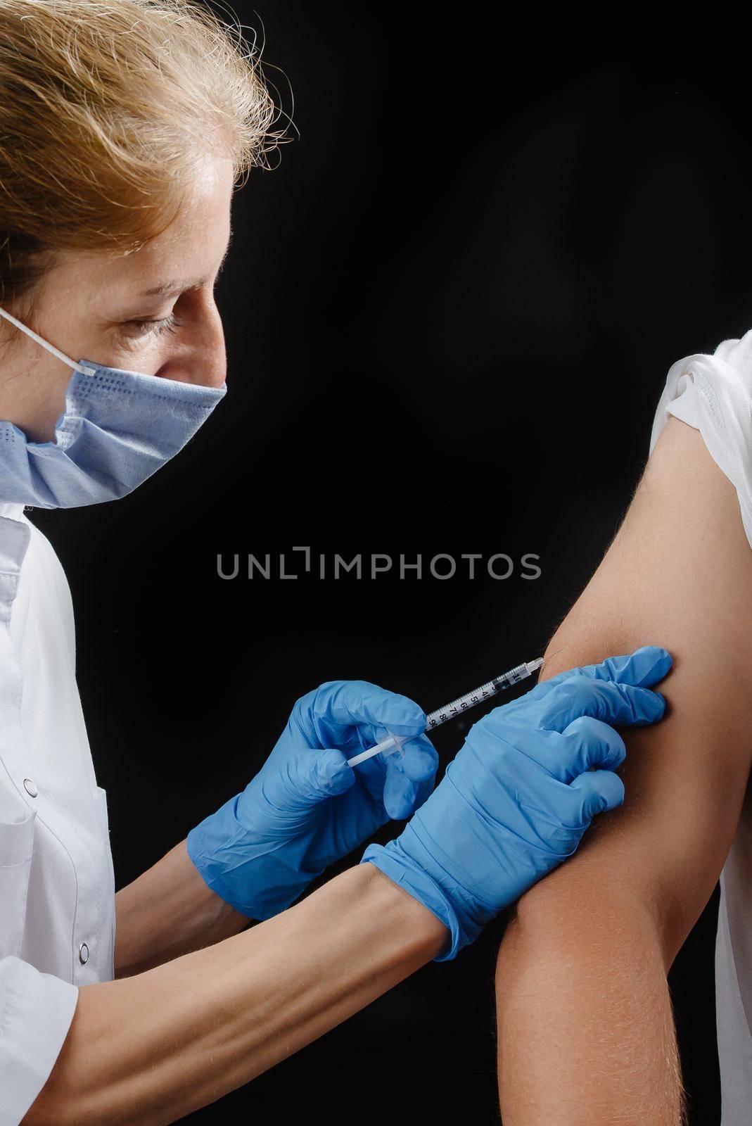 the doctor gives the shot in his hand on a black background. A female nurse vaccinates a patient.