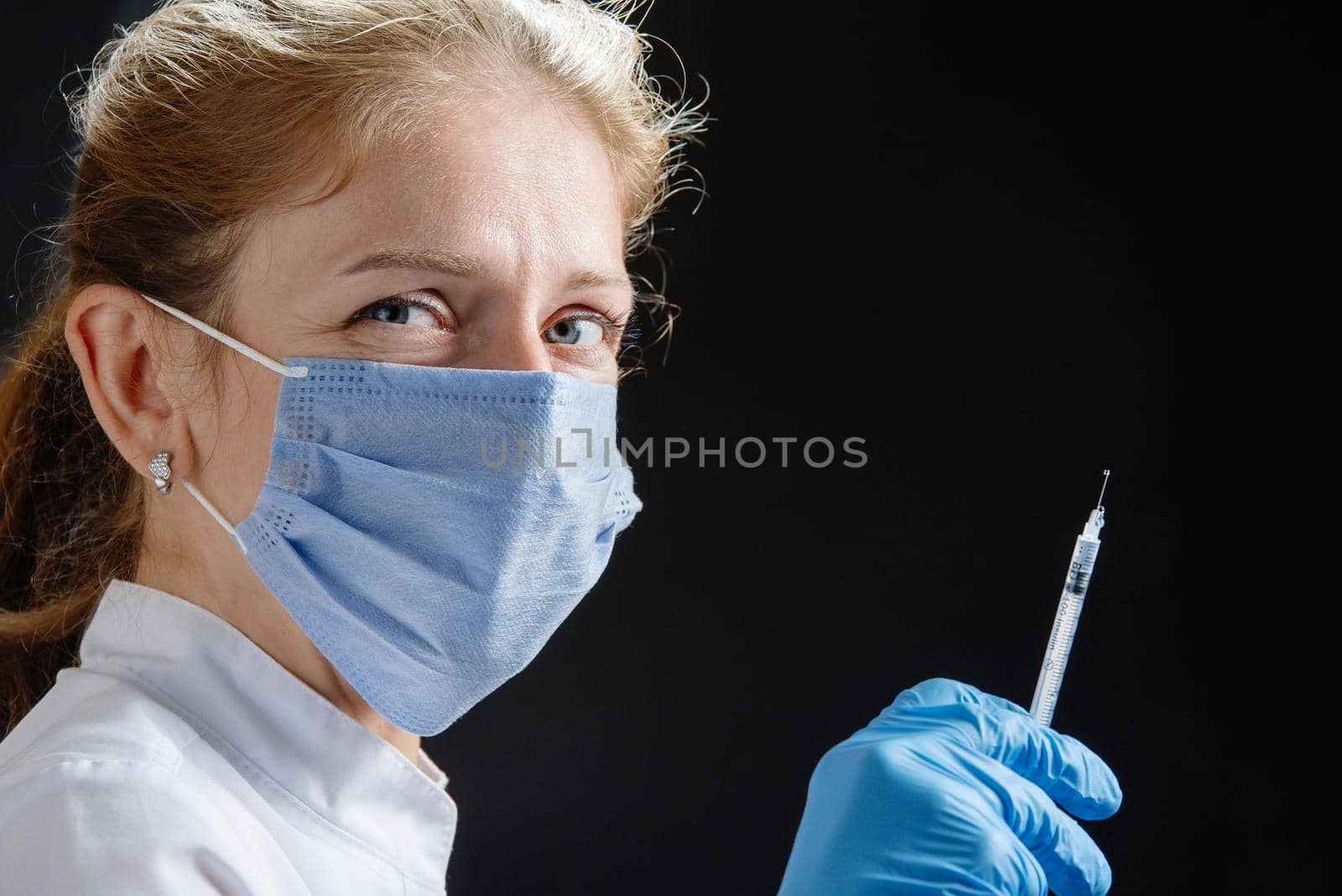 A young female doctor with a syringe looks at the camera. A nurse wearing a medical mask and blue latex gloves. Medicine and health care. Vaccination for the virus. Preventive measures against the disease. A place to copy.