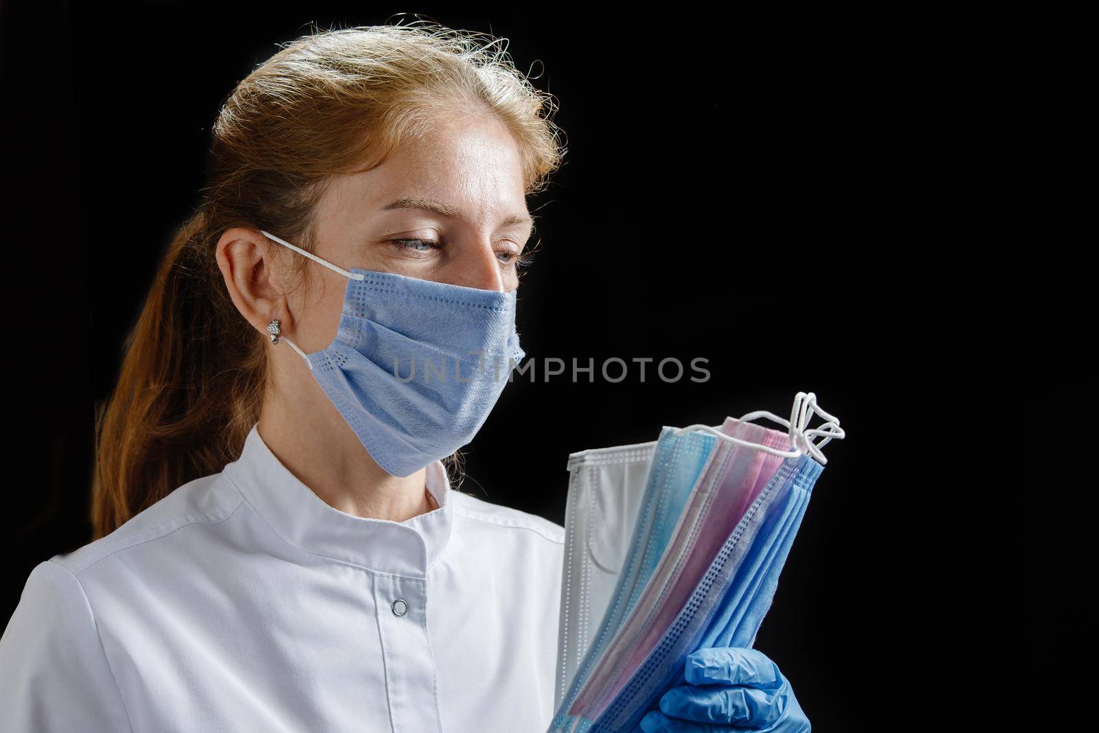 the doctor holds several masks of different colors in his hands. A nurse wearing a mask and medical gloves counts the protective disposable masks on a black background. Isolate