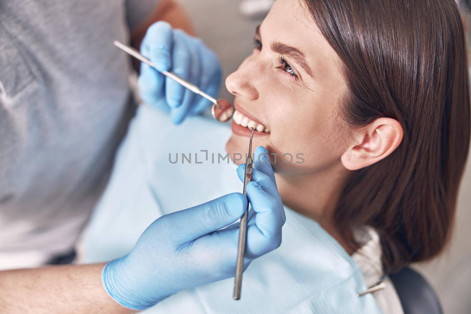 Confident mature doctor is checking teeth of young beautiful happy caucasian woman in modern clinic