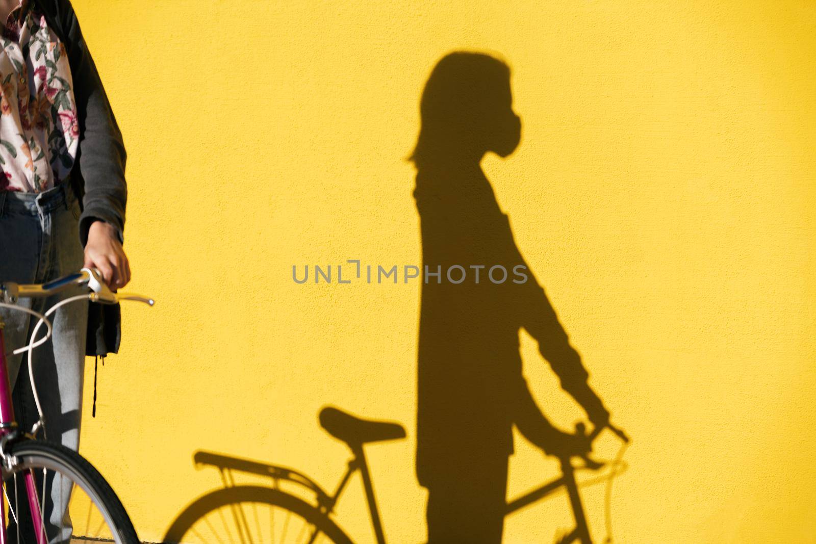 shadow of a woman on a bicycle wearing a protective mask on a colorful yellow wall, concept of protection against covid and sustainable mobility, copy space for text