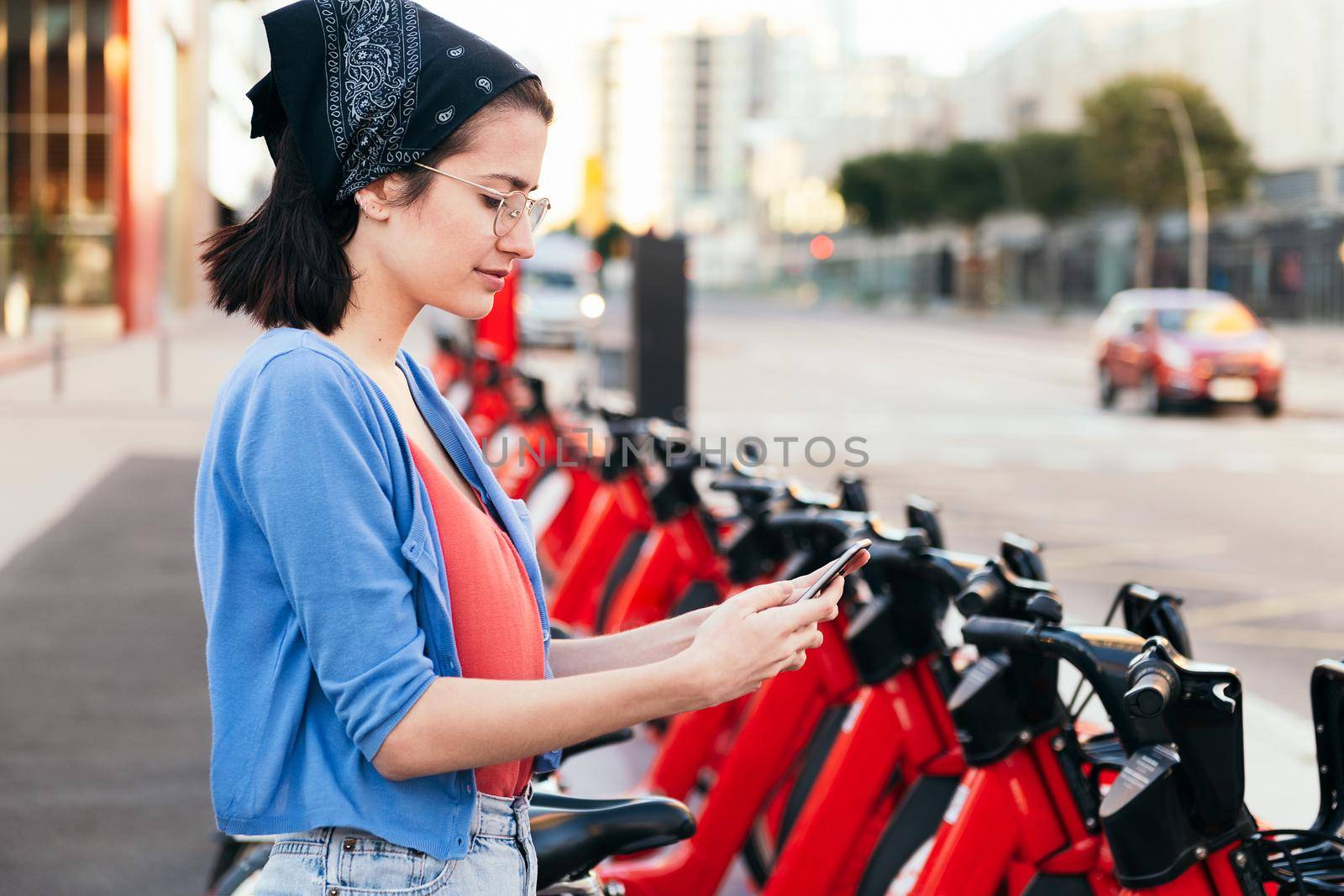 young woman using the phone next to an electric bike rental station in the city, concept of ecology and sustainable mobility against climate change, copy space for text