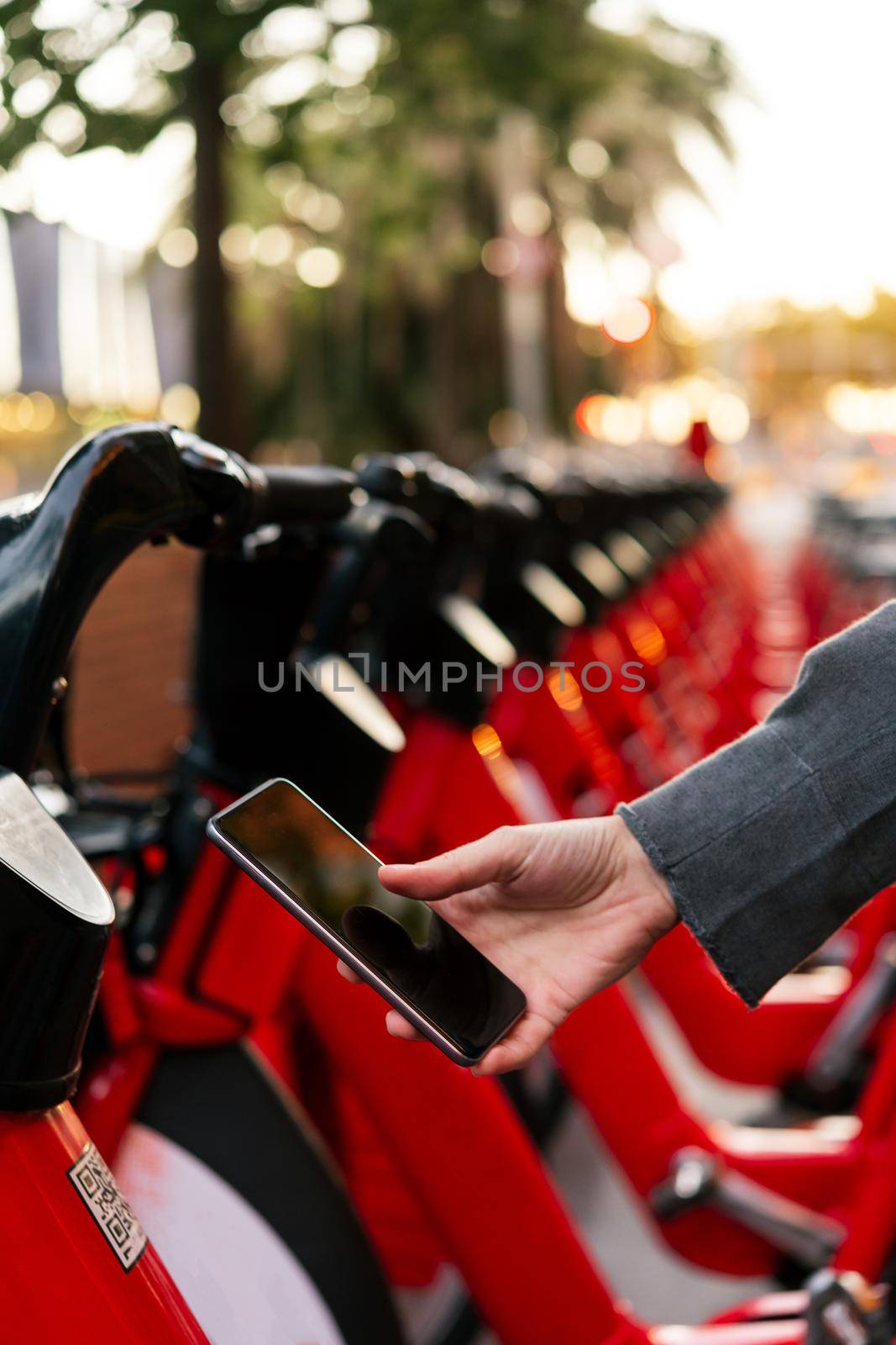 vertical photo of the detail of a hand with smart phone scanning the code to unlock the bike from the urban parking of rental bikes, concept of technology and sustainable mobility