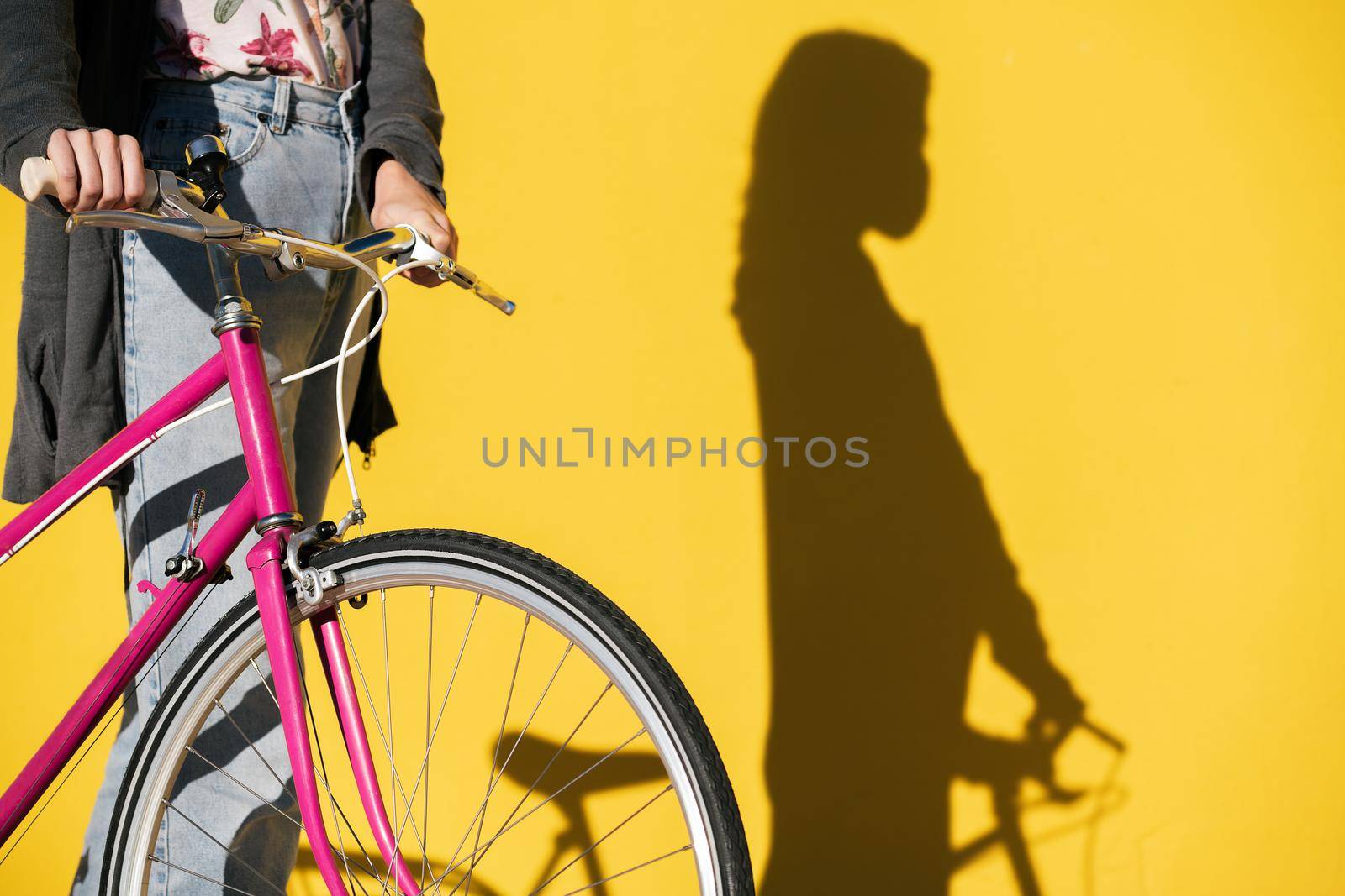 unrecognizable woman wearing mask with retro bike and her shadow on a colorful yellow wall, concept of protection against covid and sustainable mobility, copy space for text