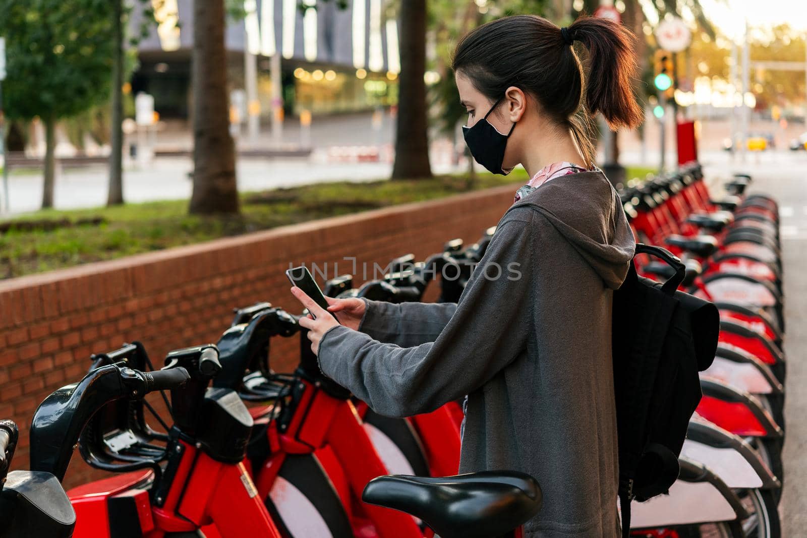 young girl with protective mask scanning the code with a smart phone to unlock a bike from the urban bike rental parking, concept of active lifestyle and sustainable mobility