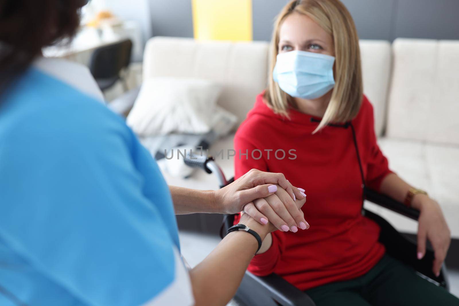 Rehabilitation doctor in protective medical mask communicates with disabled woman in wheelchair. Rehabilitation and treatment in hospice concept