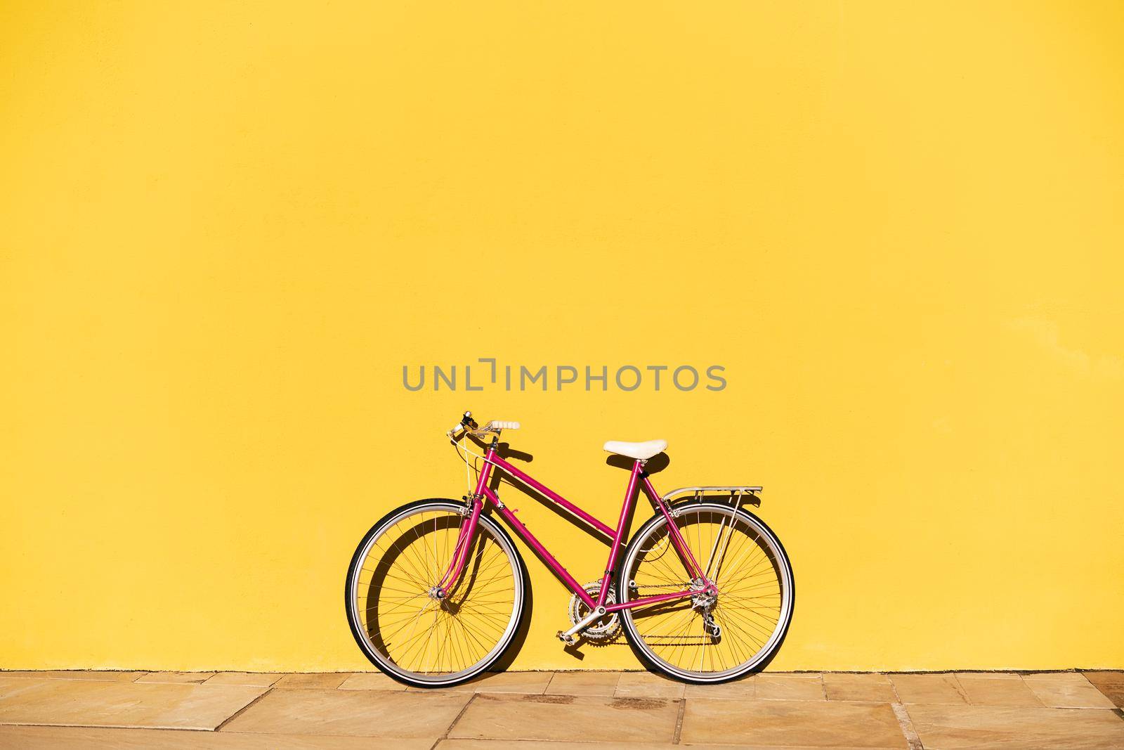 pink retro bike supported on a colorful yellow wall, concept of active lifestyle and sustainable urban mobility, copy space for text