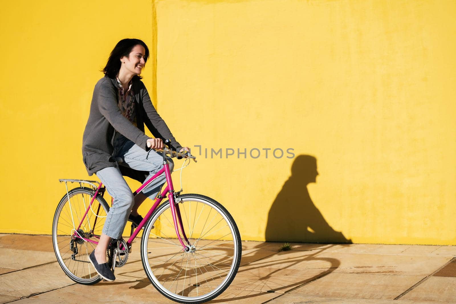 happy young teenage girl smiles as she rides her retro pink bike along a colorful yellow wall, concept of active lifestyle and sustainable mobility, copy space for text