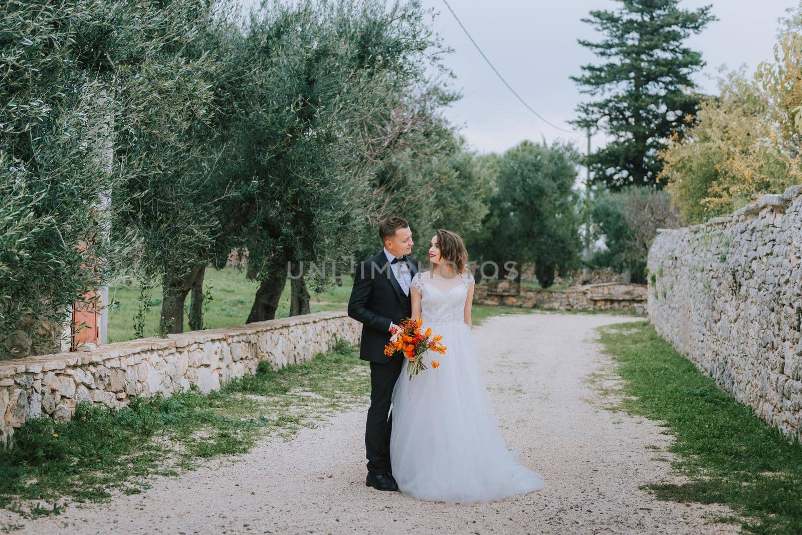 Happy stylish smiling couple walking in Tuscany, Italy on their wedding day. The bride and groom walk down the street by the hands. A stylish young couple walks. Husband and wife communicate nicely. Lovers run through the streets of the city.