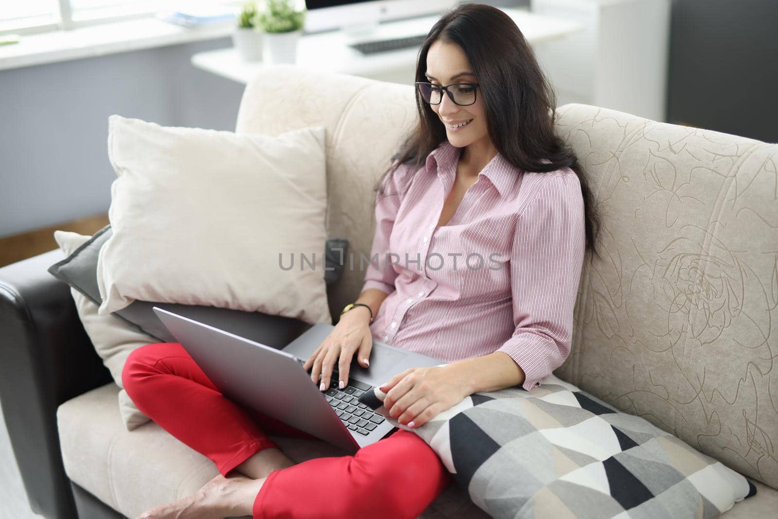 Young woman using laptop sitting on comfortable sofa in home interior. Remote work telework and freelancer concept