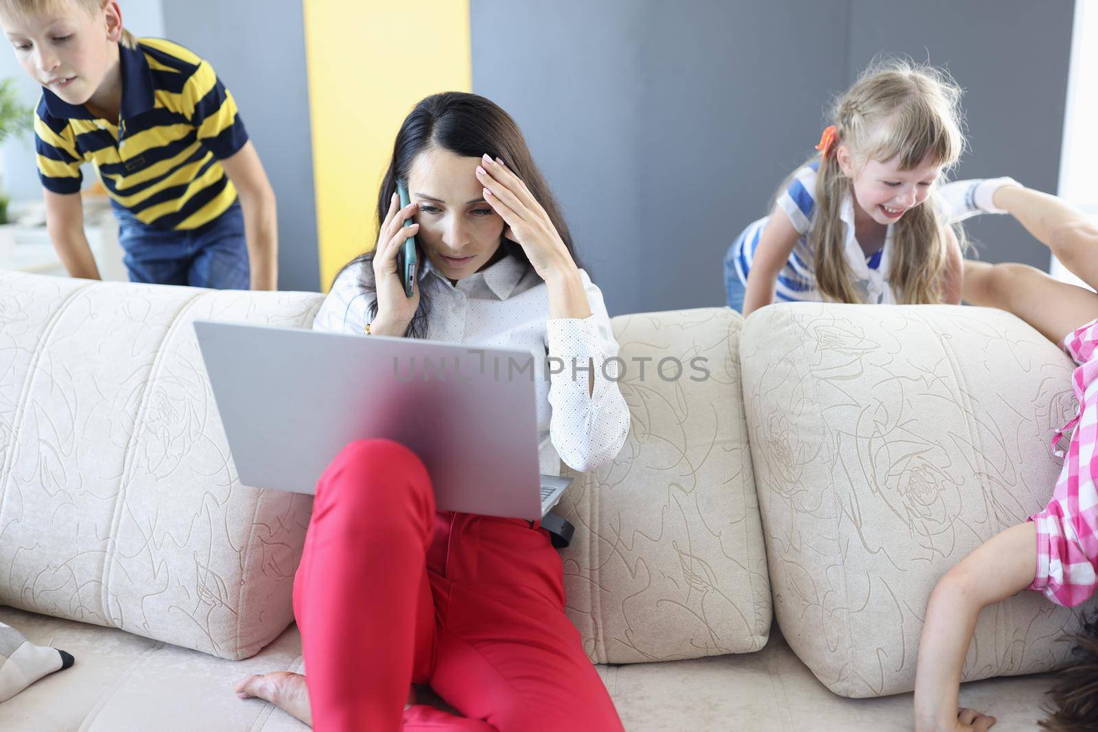 Woman working on laptop at home talking on phone and children playing. Remote work telework with kids concept