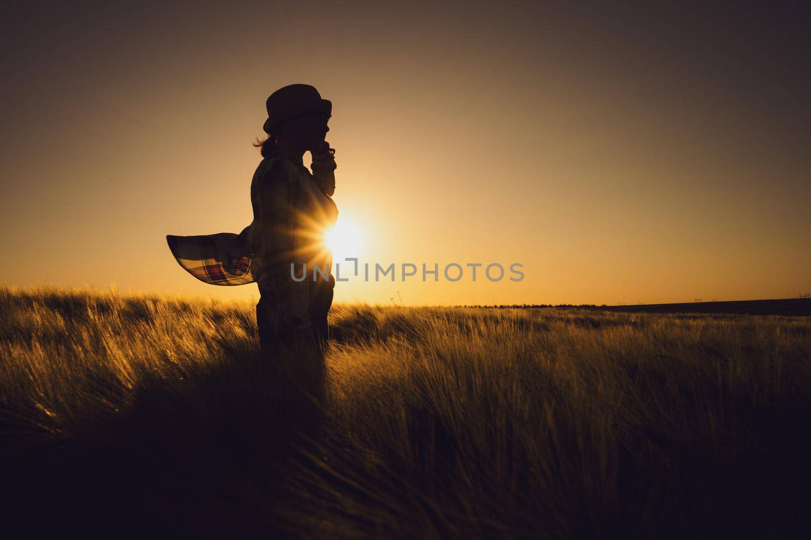 Female farmer is standing in her wheat field and enjoying sunset.