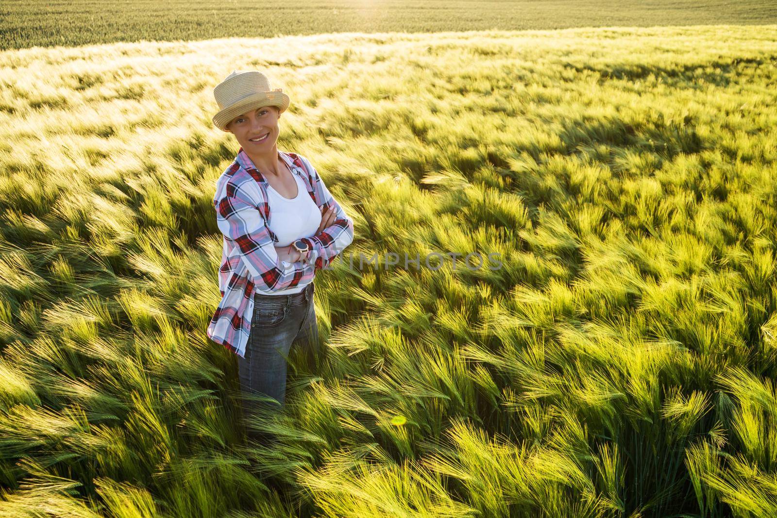 Female farmer is cultivating barley. She is smiling and looking at camera while standing in her barley field.